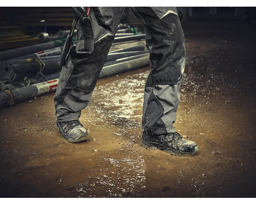 Een persoon met een werkbroek en veiligheidsschoenen staat in een plas.