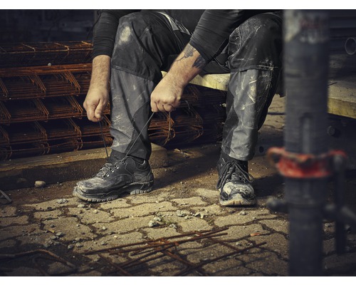 Een bouwvakker zit en knoopt zijn werkschoenen vast op een bouwplaats.