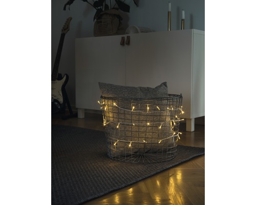 KONSTSMIDE Kerstverlichting LED lichtsnoer micro 100 lampjes extra warmwit transparant snoer 6,93 m Decoratieve scène met een mand gevuld met een lichtsnoer en een kussen op een vloerkleed