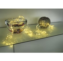 Decoratieve lichtslinger gedrapeerd rond een glazen schaal en een bolvormige vaas op een meubelstuk.