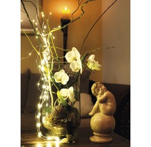 Decoratieve glazen vaas met orchideeën, takken en lichtsnoer naast een engelbeeld