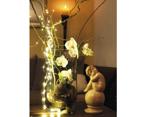 Decoratieve glazen vaas met orchideeën, takken en lichtsnoer naast een engelbeeld