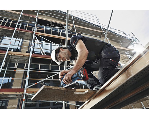 Een bouwvakker op een steiger die een houten plank bewerkt met elektrisch gereedschap.