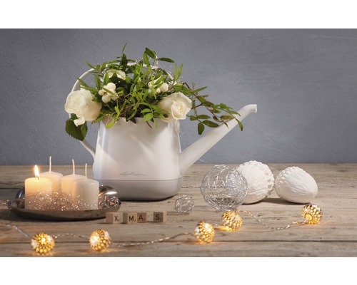 Decoratieve gieter met bloemstuk, kaarsen, ballen en lichtslinger op een houten tafel