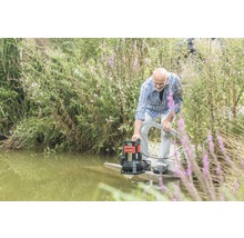 Man bedient een vuilwaterpomp aan de oever van een waterpartij.