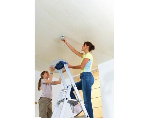 Vrouw op een ladder die een lamp aan een houten plafond bevestigt, met een kind dat helpt