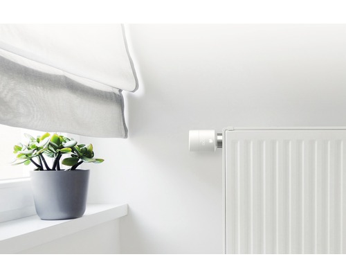 Radiator met elektronische thermostaat, gordijn en kamerplant op vensterbank