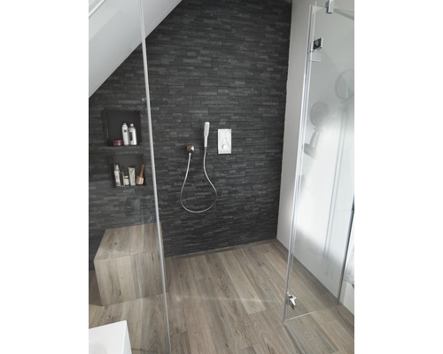 Badkamer met douche, stenen muur en houten vloer.