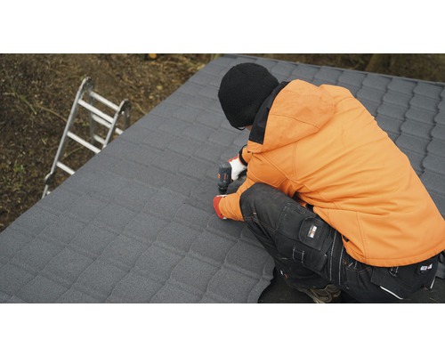 Ambachtsman bevestigt dakplaten met een accuschroevendraaier op een dak