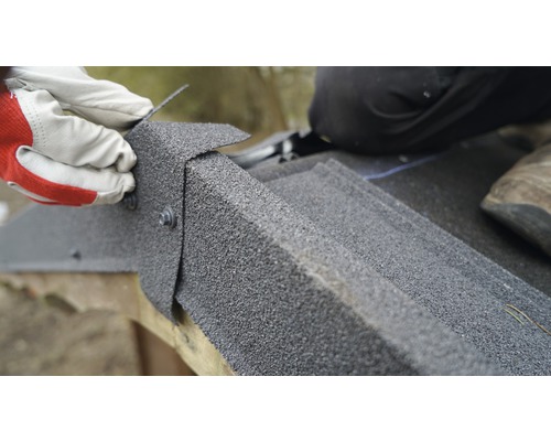 Close-up van de installatie van dakshingles met schroeven door een persoon met handschoenen.