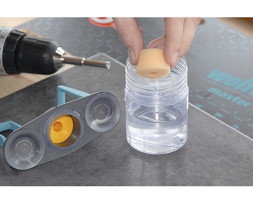 Tegelgereedschap in gebruik met spons, container met reinigingsvloeistof en boormachine