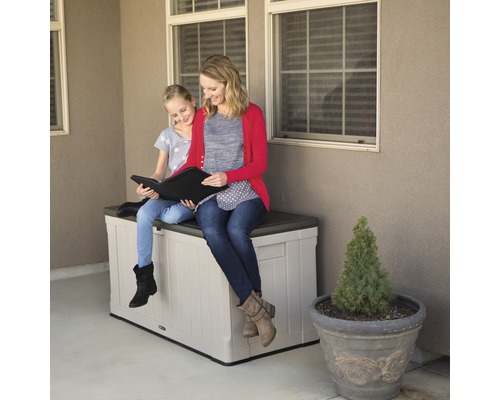 Een vrouw en een meisje zitten op een opbergbox buiten en kijken naar een boek.