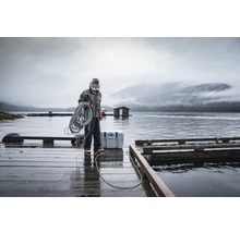 Man met touw op een houten steiger aan het water met een koelbox