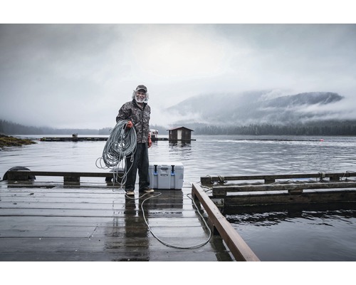 Man met touw op een houten steiger aan het water met een koelbox