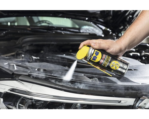Toepassing van WD-40 siliconenspray in de motorruimte van een auto.