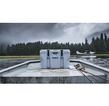 Koelbox op een boot met vishengels en een watervliegtuig op de achtergrond