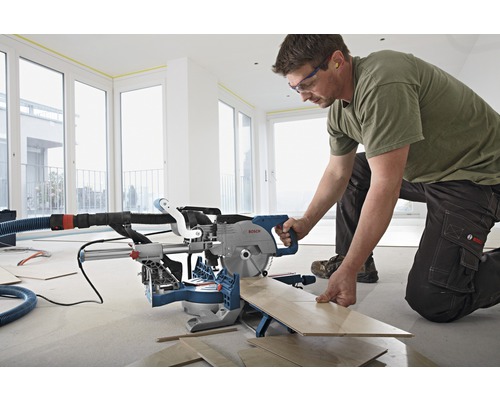 Een man gebruikt een afkortzaag om hout te zagen in een heldere kamer.