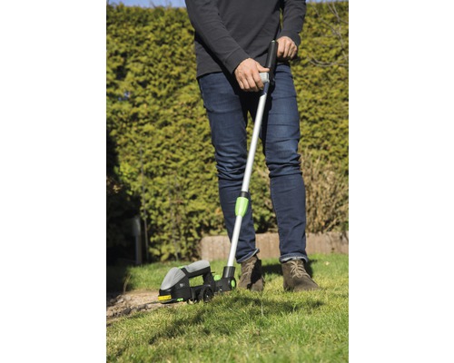 Een persoon gebruikt een graskantensnijder voor gazononderhoud in de tuin.