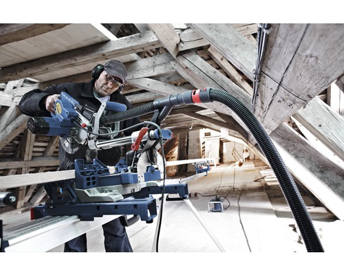 Een persoon werkt met een verstekzaag en stofzuiger in een dakconstructie.