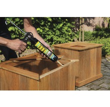 Persoon brengt lijm aan met een kitpistool op een houten plantenbak.