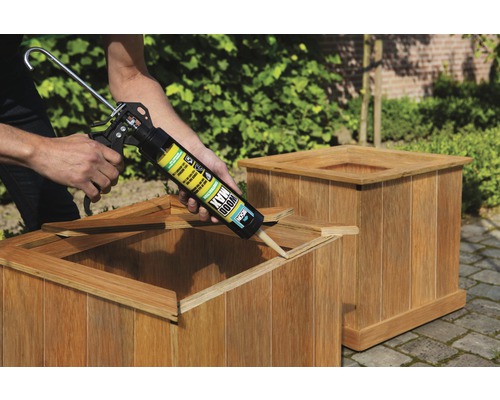 Persoon brengt lijm aan met een kitpistool op een houten plantenbak.
