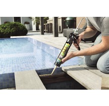 Iemand gebruikt een kitpistool met montagelijm op een houten terras bij een zwembad.