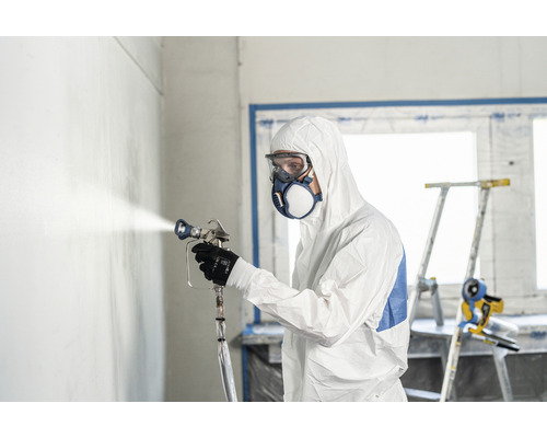 Man met beschermend pak, veiligheidsbril en masker spuit een muur met een verfspuitpistool