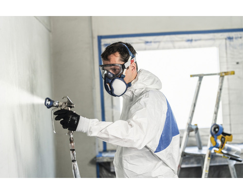 Man met beschermend pak en ademhalingsmasker die verf op een muur spuit