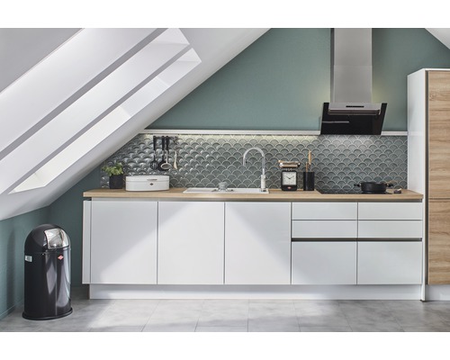 Keuken met witte kasten, wastafel, afzuigkap en vuilnisemmer onder een dakraam