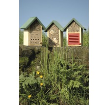 Drie houten insectenhotels op een muur met planten op de voorgrond.