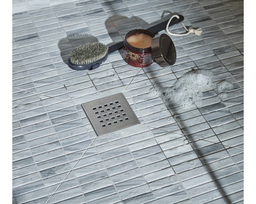 Detailopname van een douche met vloertegels, doucheputje, borstel, badadditief en zeepschuim