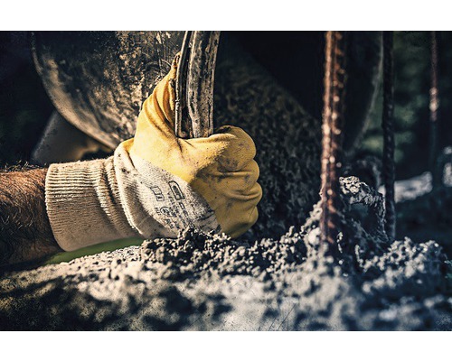 Een hand met een werkhandschoen houdt gereedschap vast in de buurt van betonstaal.