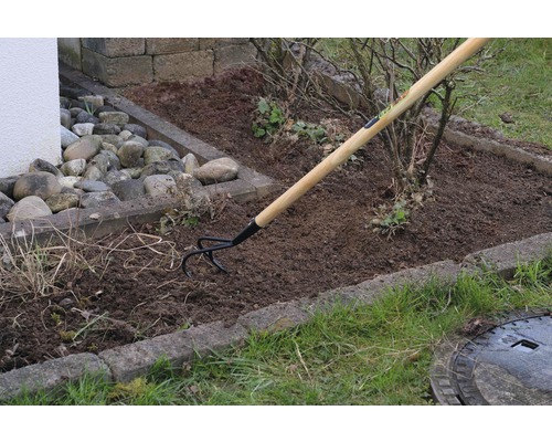 Tuinhark met houten steel in gebruik voor het bewerken van de grond in een tuinperk.
