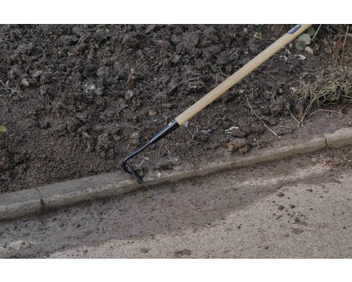 Tuinhacke met houten handvat in gebruik naast een stoeprand