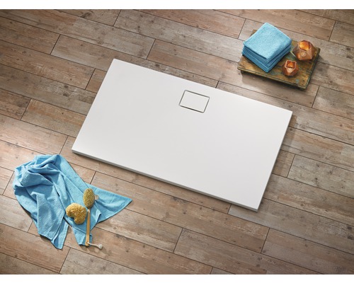 Rechthoekige, witte douchebak met afvoergarnituur op houten vloer