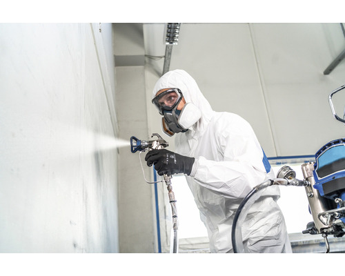 Persoon met beschermend pak en ademhalingsmasker spuit met een verfspuitpistool