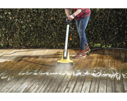 Een persoon reinigt een houten terras met een elektrische terrasreiniger.