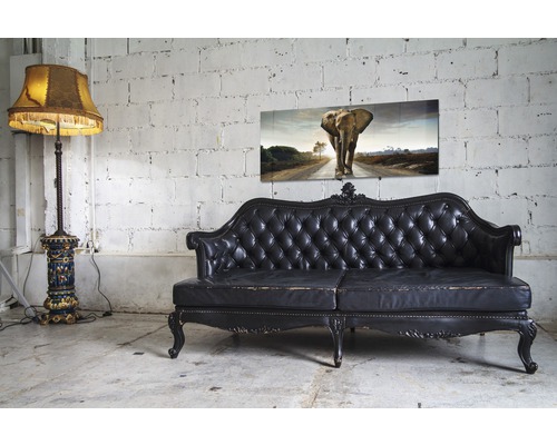 Decoratieve scène met staande lamp, leren bank en muurkunst met olifantenmotief voor een bakstenen muur