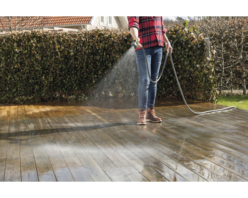 Een persoon maakt een houten terras schoon met een waterslang.