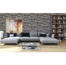 Woonkamer met grijze bank, boekenkast en bakstenen muur.