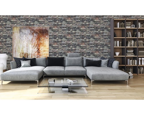 Woonkamer met grijze bank, boekenkast en bakstenen muur.