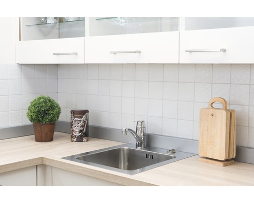 Keukenscène met spoelbak, kraan, snijplanken en decoratie op een licht aanrechtblad voor een witte tegelwand