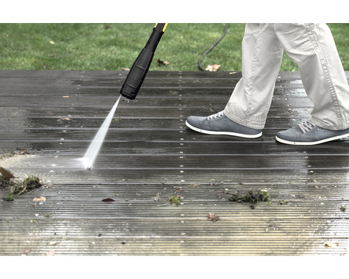 Een persoon reinigt een houten terras met een hogedrukreiniger.