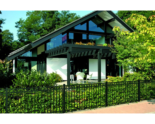 Modern huis met glazen gevel, omgeven door een zwart hek en weelderig groen