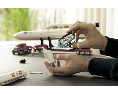 Handen lijmen een model met secondelijm in elkaar. Op de achtergrond is een speelgoedvrachtwagen met oplegger te zien.