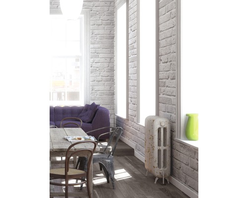 Lichte woonkamer met eettafel, stoelen, bank en radiator tegen een bakstenen muur