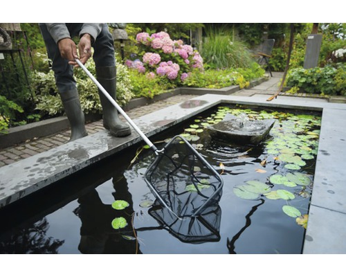 Persoon met vijvernet bij een tuinvijver met waterlelies en een fontein