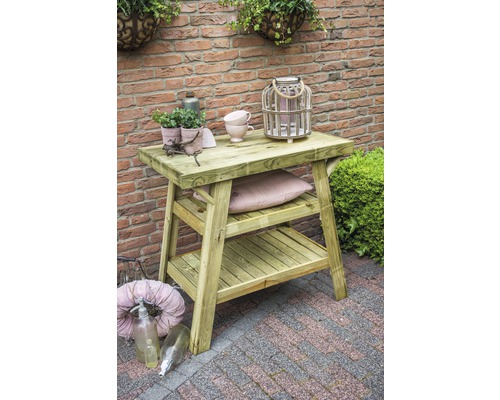 Tuinscene met een houten tafel met twee planken, gedecoreerd met planten en serviesgoed voor een bakstenen muur