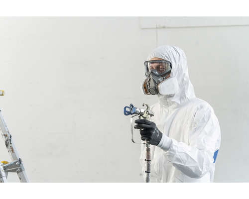 Een persoon in beschermende kleding, veiligheidsbril en ademhalingsmasker houdt een verfspuitpistool vast.