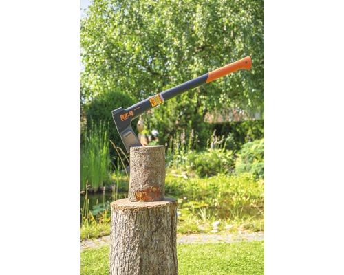 For.q logo. Een bijl steekt in een houtblok in de tuin.